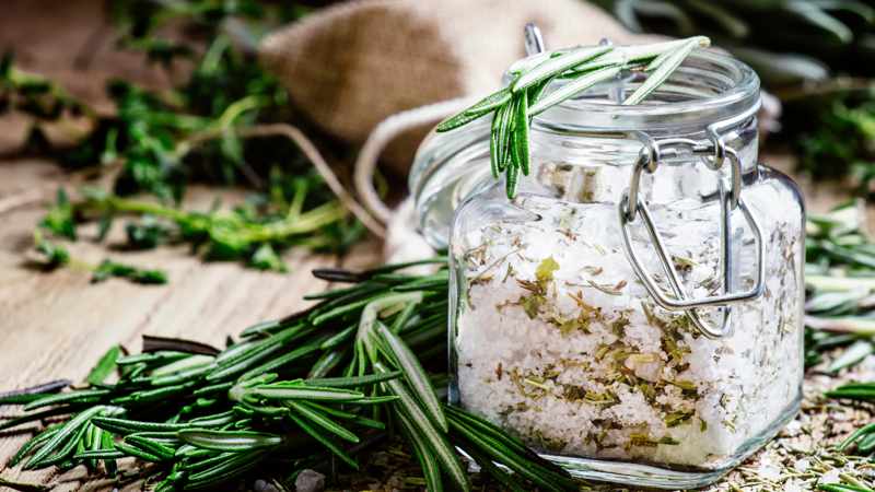Bügelglas mit Kräutersalz vor Dekoration aus frischen Kräutern